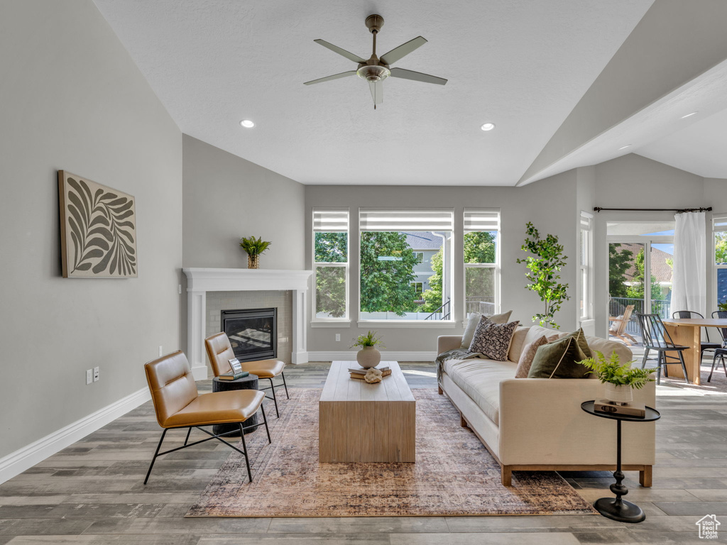 Living area featuring vaulted ceiling, plenty of natural light, wood finished floors, a glass covered fireplace, and a ceiling fan