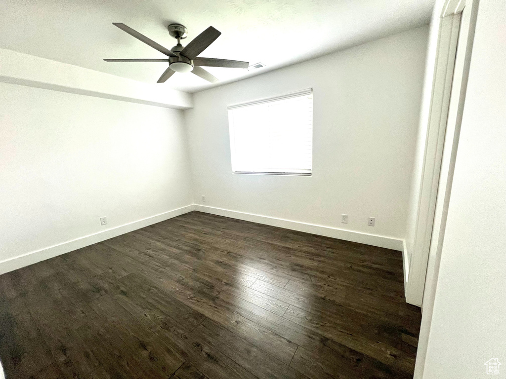 Empty room featuring dark wood-style flooring, a ceiling fan, and baseboards