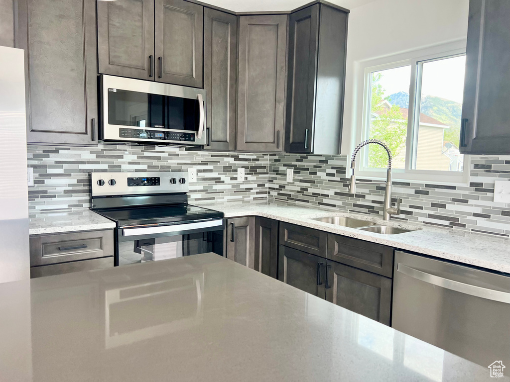 Kitchen featuring stainless steel appliances, a sink, backsplash, and light stone counters