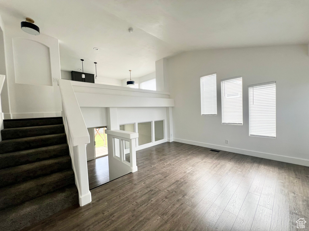 Unfurnished living room with lofted ceiling, healthy amount of natural light, dark wood-style floors, and baseboards