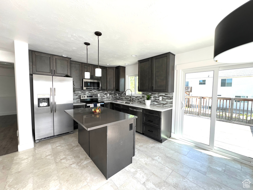 Kitchen with stainless steel appliances, tasteful backsplash, a sink, a kitchen island, and decorative light fixtures