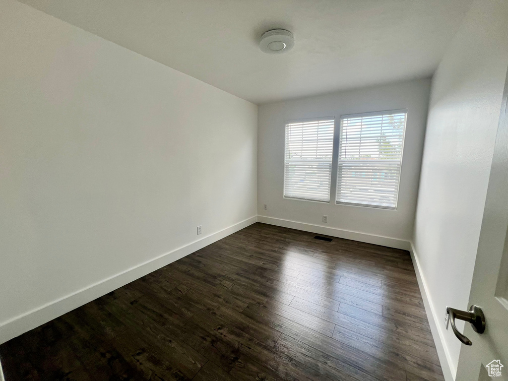 Empty room featuring baseboards and dark wood-style flooring