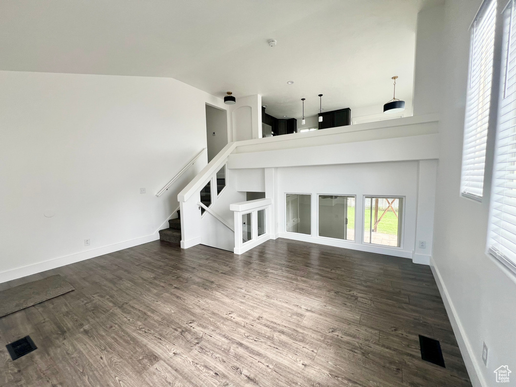 Unfurnished living room with dark wood-style flooring, stairway, baseboards, and a high ceiling