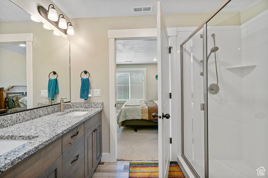 Full bath with connected bathroom, a shower stall, double vanity, a textured ceiling, and wood finished floors