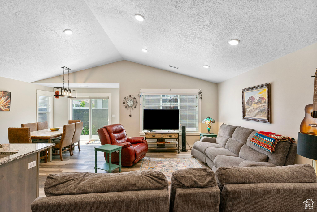 Living area featuring lofted ceiling, light wood-type flooring, and a textured ceiling