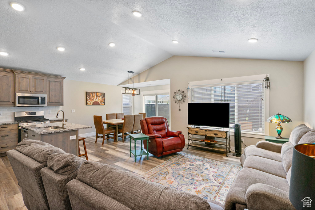 Living area with lofted ceiling, light wood-style floors, a textured ceiling, baseboards, and recessed lighting