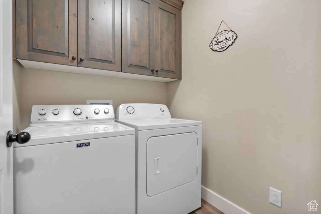 Laundry area featuring cabinet space, washer and dryer, baseboards, and wood finished floors