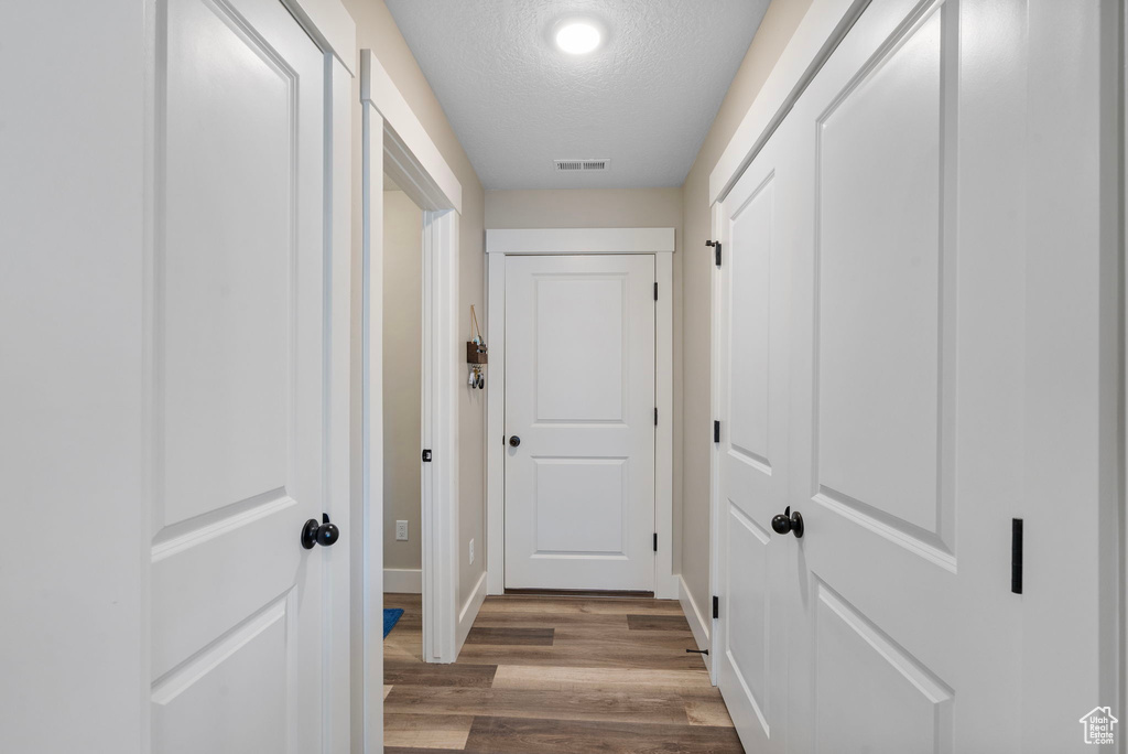 Hallway with a textured ceiling, wood finished floors, and baseboards