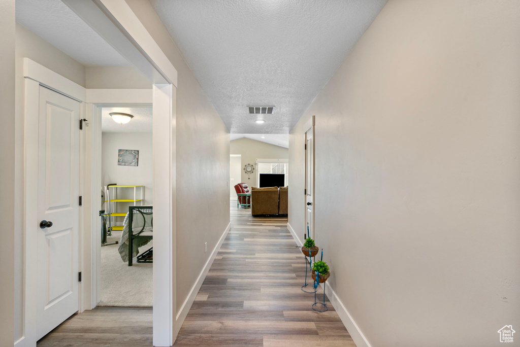 Hall with a textured ceiling, wood finished floors, and baseboards