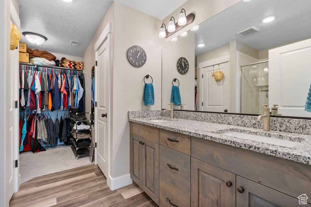 Bathroom with wood finished floors, a textured ceiling, double vanity, a stall shower, and a walk in closet