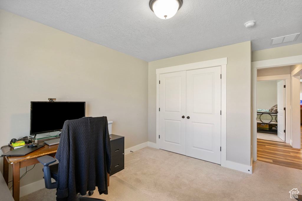 Office space with baseboards, light carpet, and a textured ceiling
