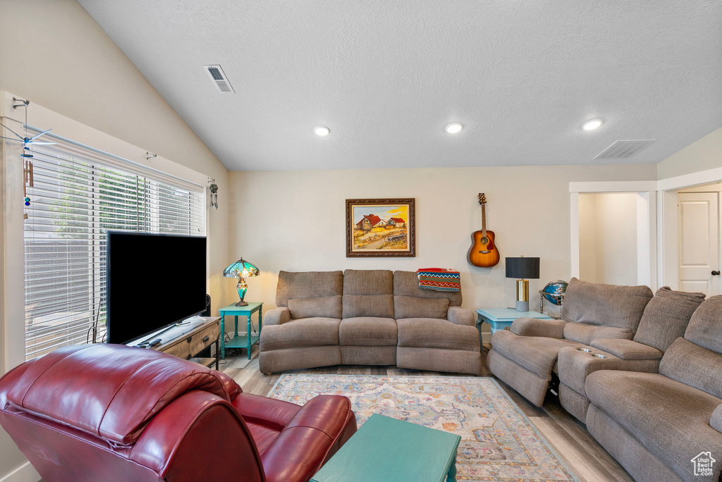 Living room with wood finished floors, recessed lighting, lofted ceiling, and a textured ceiling