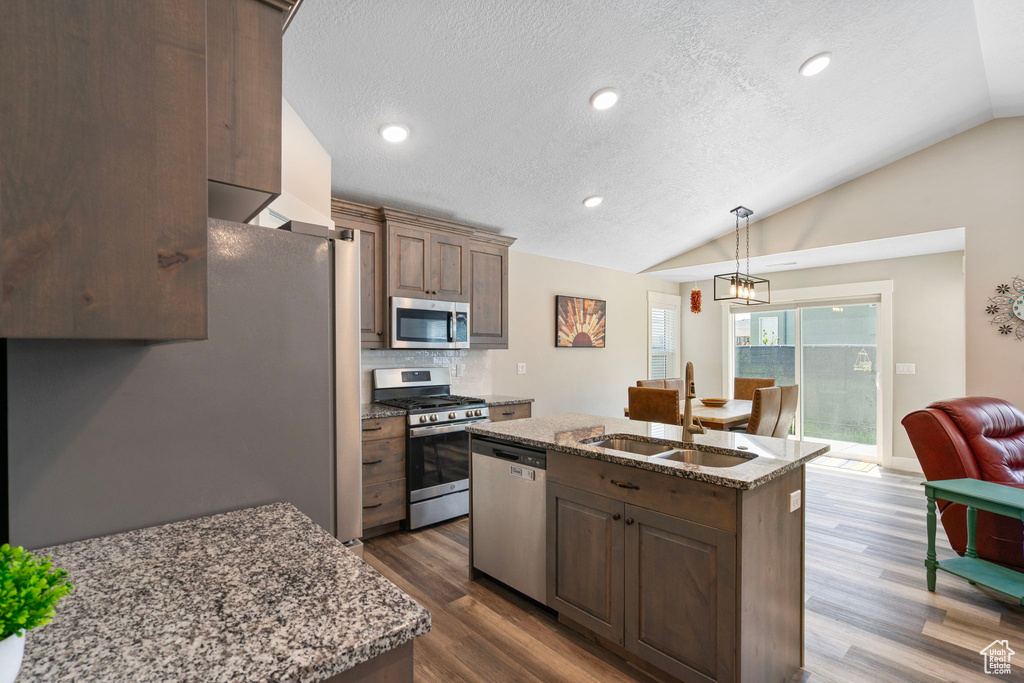 Kitchen featuring stainless steel appliances, a sink, vaulted ceiling, a kitchen island with sink, and dark wood-style flooring