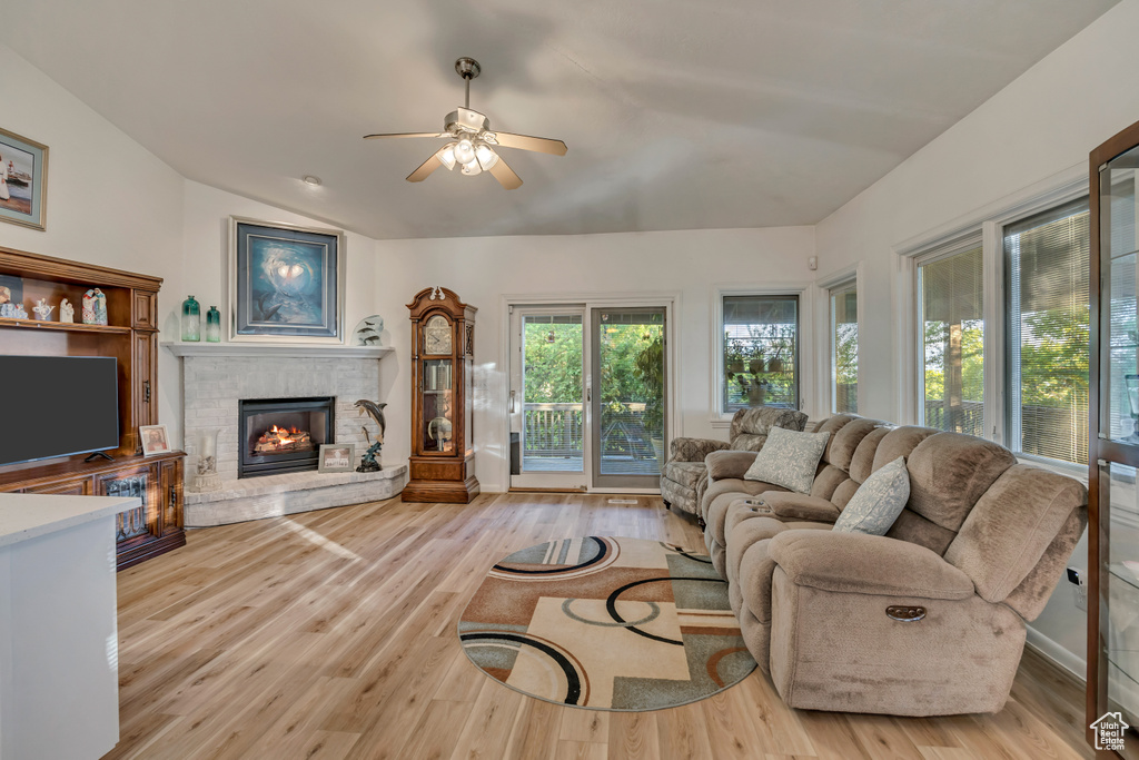 Living room with a stone fireplace, ceiling fan, light wood-type flooring, and vaulted ceiling