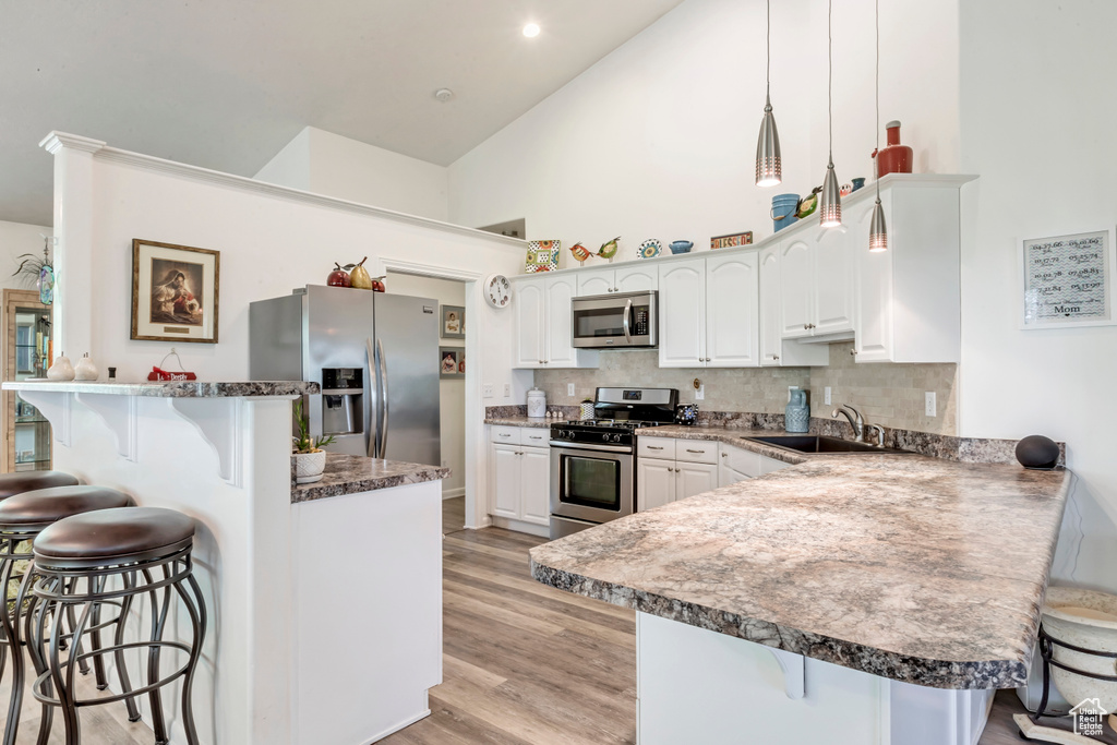 Kitchen with appliances with stainless steel finishes, a kitchen bar, a peninsula, high vaulted ceiling, and a sink