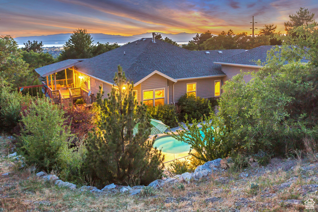 Back of property at dusk with roof with shingles, an outdoor pool, and a deck