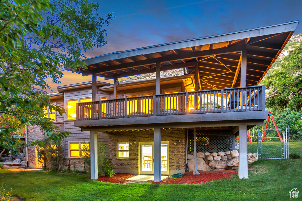 Back of house featuring a yard, a wooden deck, a gate, and brick siding
