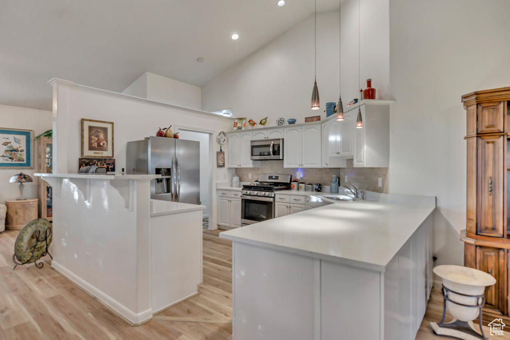 Kitchen with appliances with stainless steel finishes, a peninsula, a sink, high vaulted ceiling, and light countertops