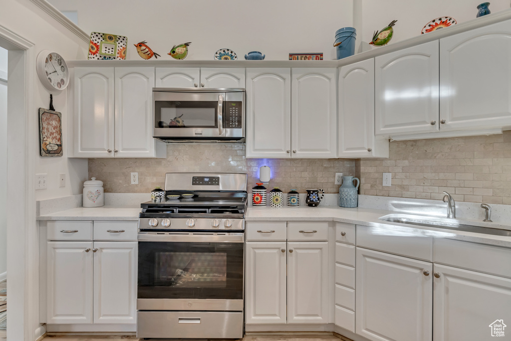 Kitchen with appliances with stainless steel finishes, a sink, light countertops, and white cabinetry