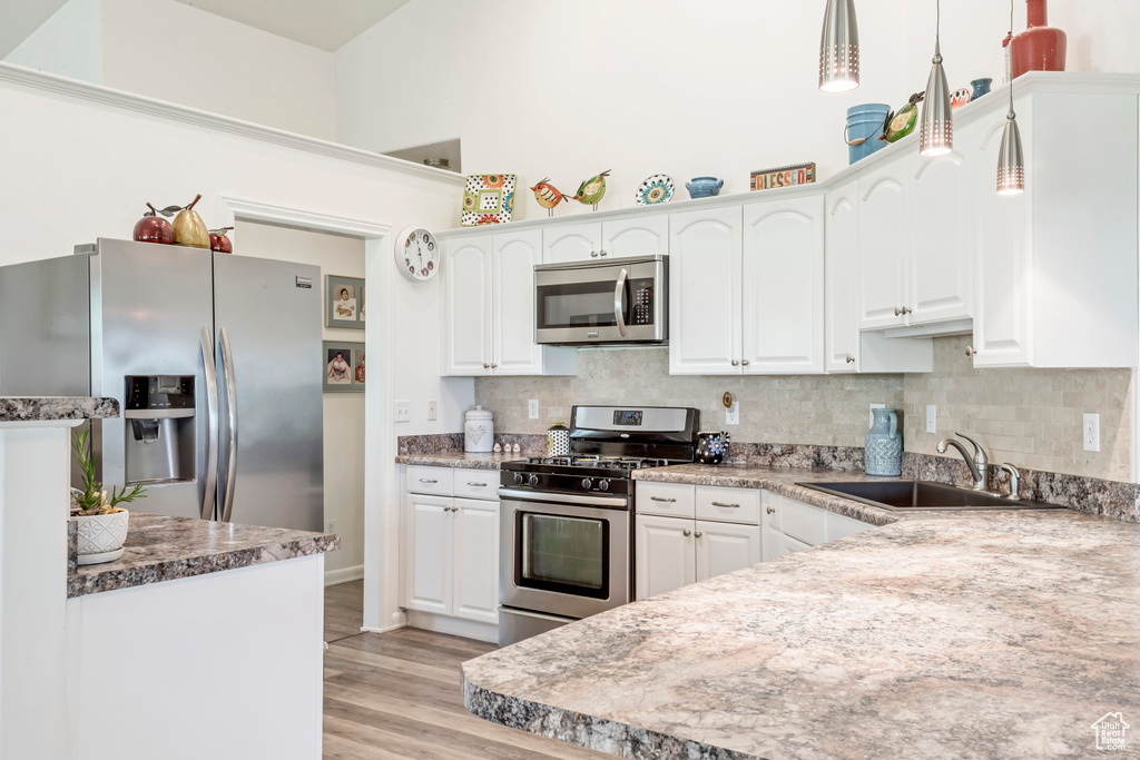 Kitchen featuring stainless steel appliances, a sink, white cabinetry, light wood-style flooring, and a high ceiling