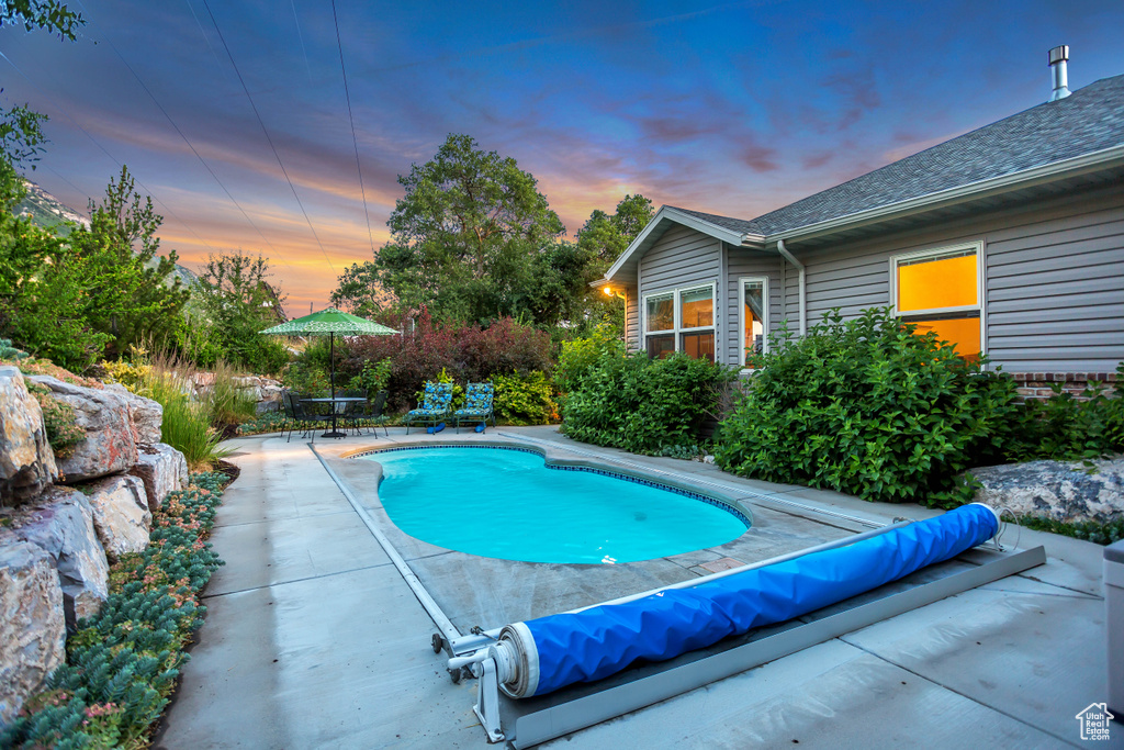 Pool at dusk featuring a patio and a covered pool