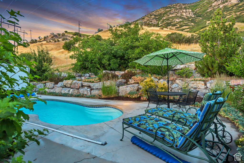 Pool at dusk featuring a patio area, a mountain view, an outdoor pool, and outdoor dining area
