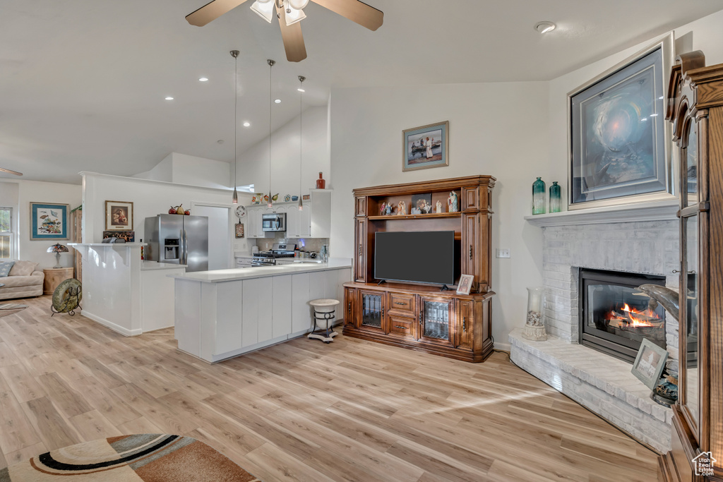 Living area with a ceiling fan, light wood-style floors, a fireplace, high vaulted ceiling, and recessed lighting