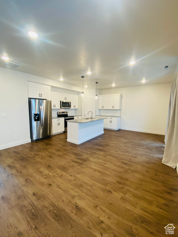 Kitchen featuring appliances with stainless steel finishes, open floor plan, an island with sink, white cabinetry, and dark wood-type flooring