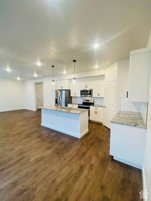 Kitchen featuring stainless steel appliances, white cabinets, dark wood-type flooring, backsplash, and an island with sink