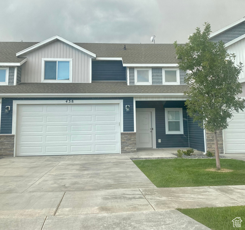 Townhome / multi-family property featuring stone siding, concrete driveway, a shingled roof, and a garage