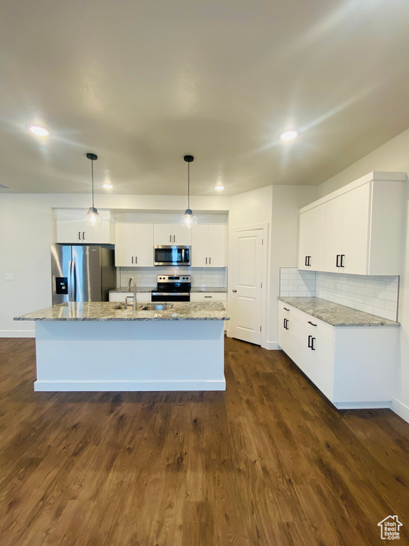 Kitchen featuring stainless steel appliances, a sink, tasteful backsplash, white cabinetry, and a kitchen island with sink