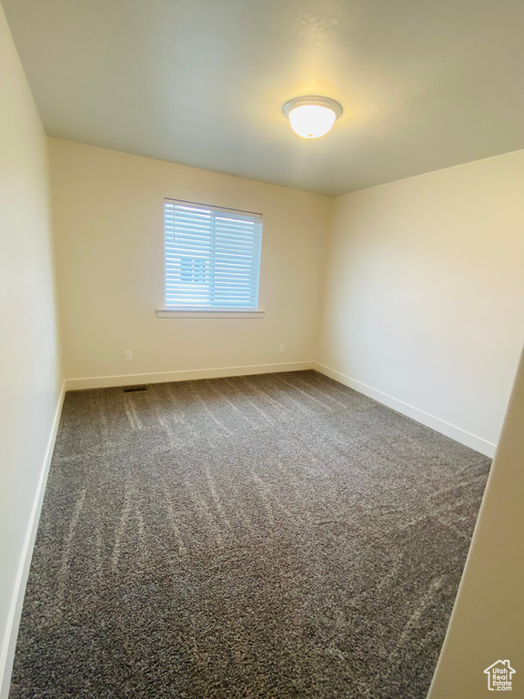 Empty room featuring baseboards and dark colored carpet