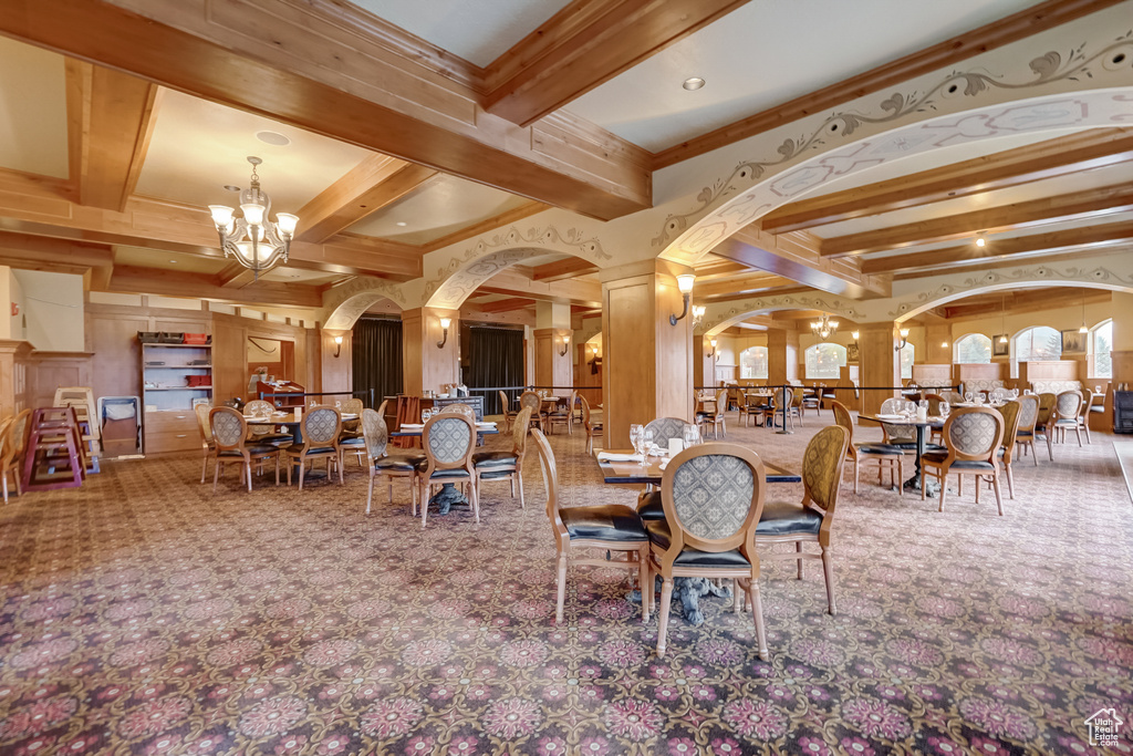 Dining area featuring carpet, a chandelier, beamed ceiling, ornate columns, and crown molding
