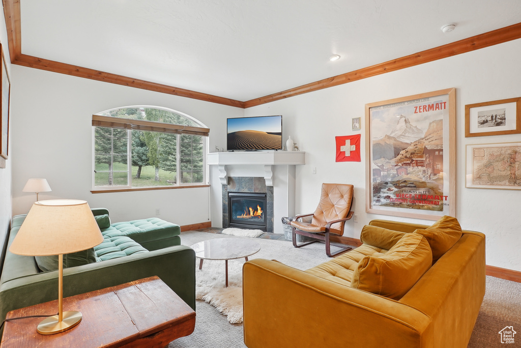 Living room with baseboards, a tiled fireplace, crown molding, and carpet flooring
