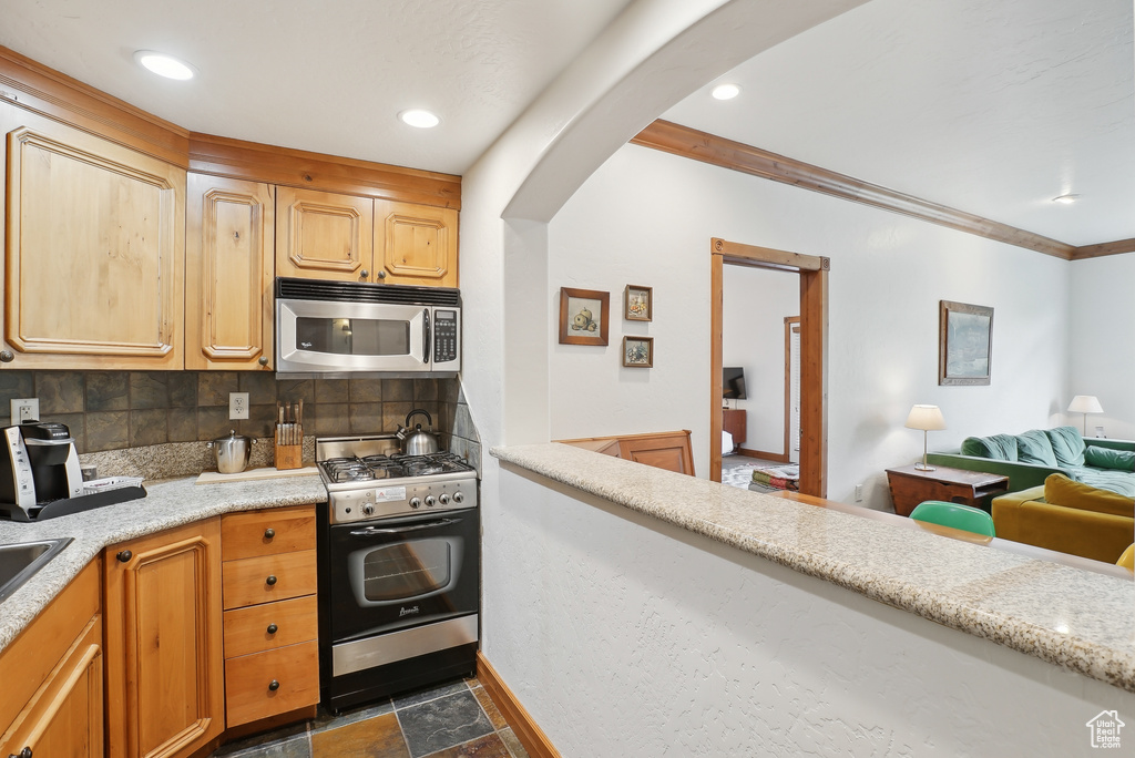 Kitchen with stainless steel appliances, arched walkways, light countertops, decorative backsplash, and crown molding