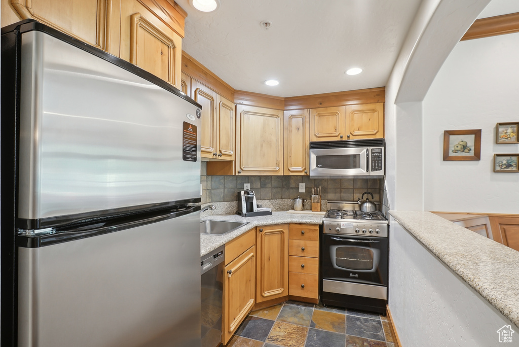 Kitchen featuring appliances with stainless steel finishes, stone finish floors, light countertops, backsplash, and a sink