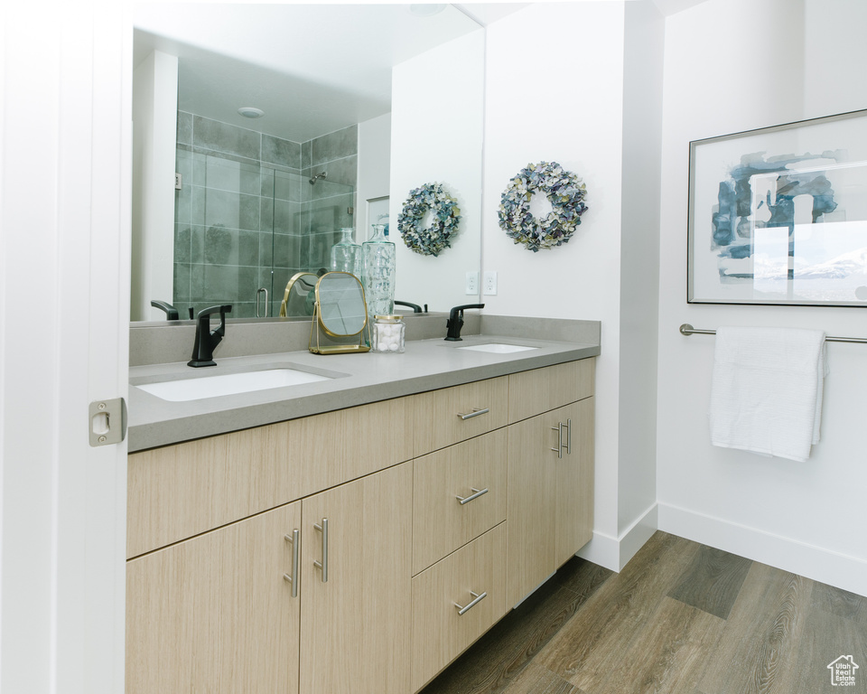 Full bath featuring double vanity, wood finished floors, a tile shower, and baseboards