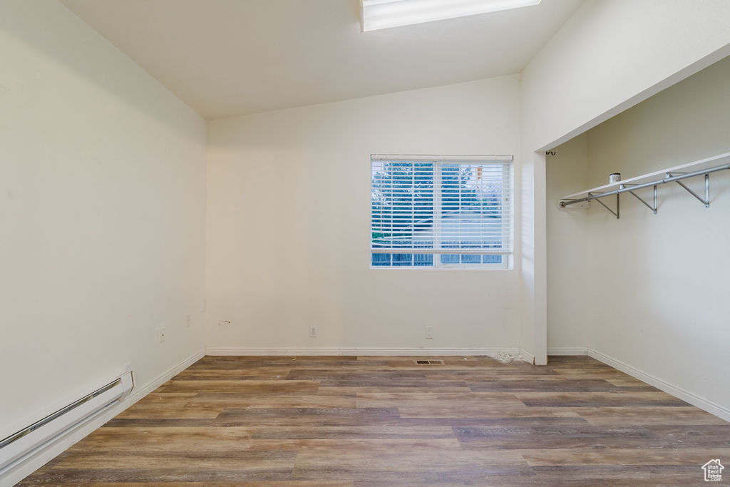 Unfurnished bedroom with baseboard heating, vaulted ceiling, wood finished floors, and baseboards