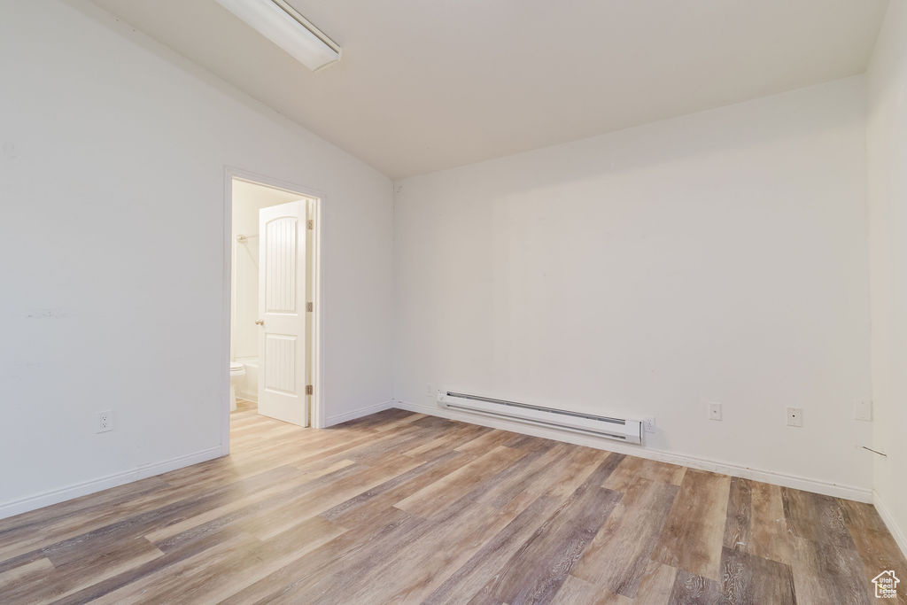 Spare room with baseboard heating, wood finished floors, vaulted ceiling, and baseboards