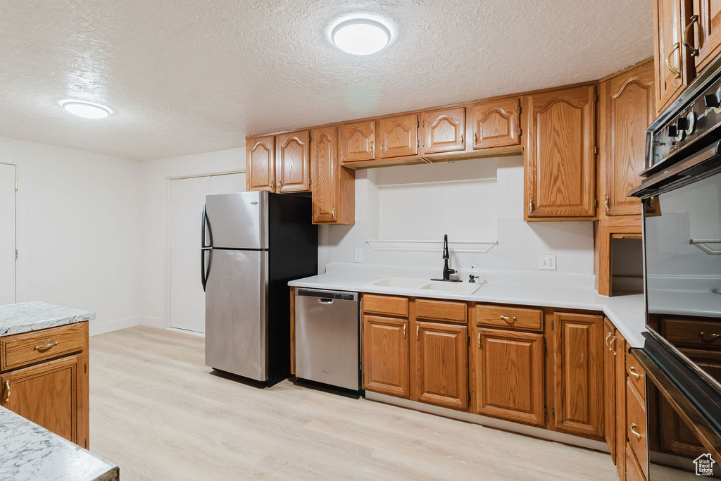 Kitchen featuring stainless steel appliances, a sink, light wood-style flooring, light countertops, and a textured ceiling
