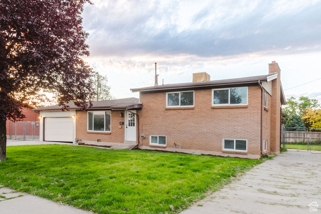 Split level home featuring a chimney, brick siding, a garage, and driveway
