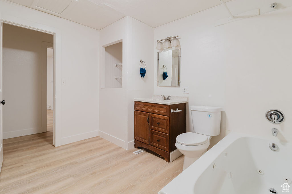 Bathroom with a jetted tub, wood finished floors, vanity, toilet, and baseboards