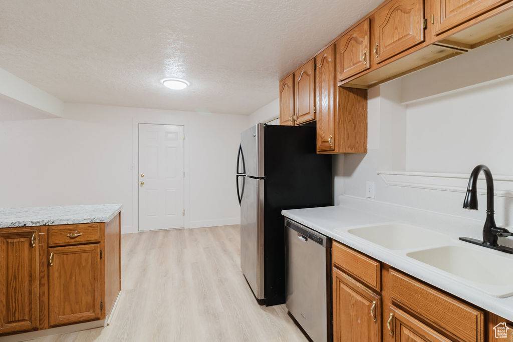 Kitchen featuring appliances with stainless steel finishes, a sink, light wood-type flooring, light countertops, and brown cabinetry