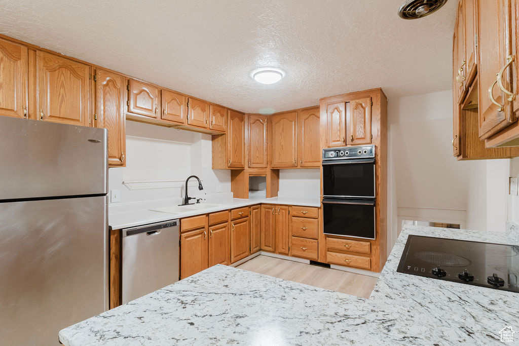 Kitchen featuring black appliances, a textured ceiling, light wood-style floors, light countertops, and a sink