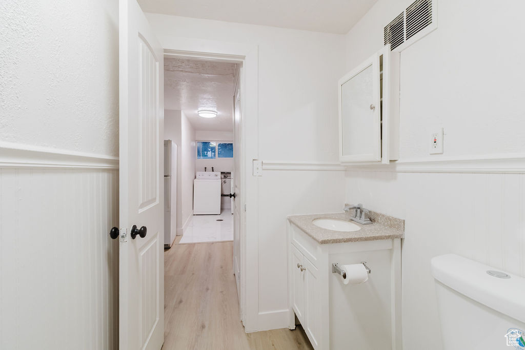 Bathroom featuring vanity, washer / clothes dryer, wood finished floors, toilet, and a wainscoted wall