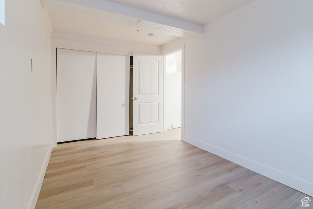 Unfurnished bedroom featuring light wood-style flooring, baseboards, a closet, and ornamental molding