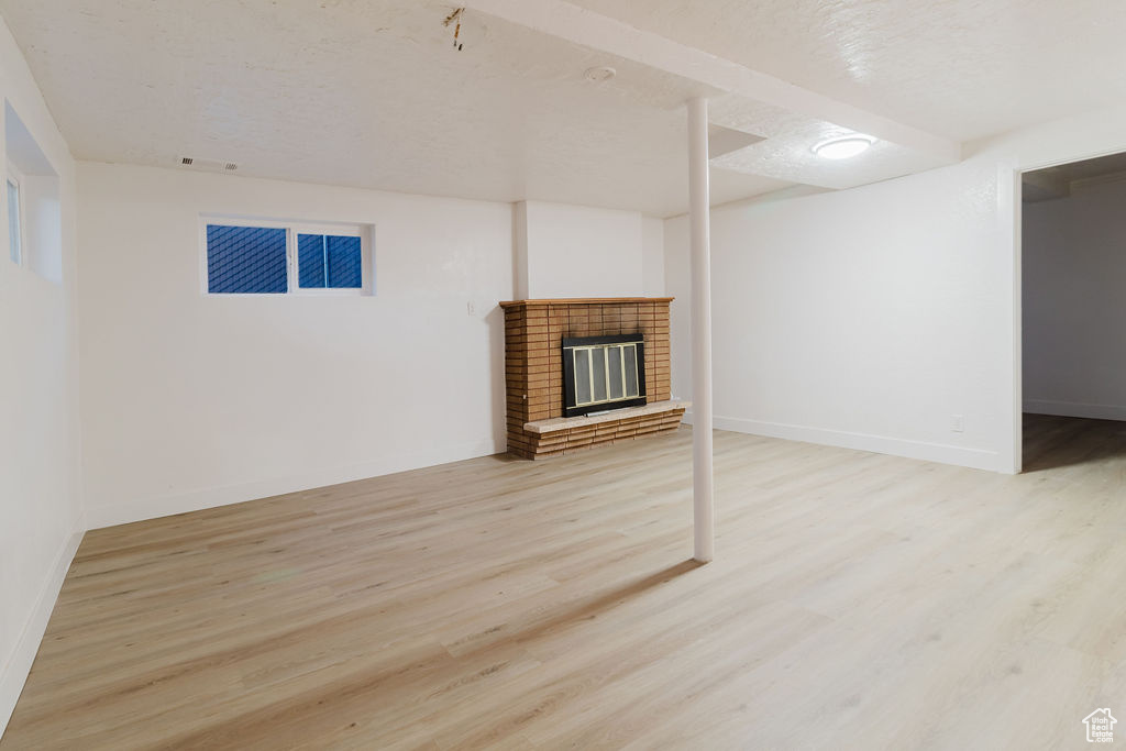 Unfurnished living room featuring light wood-type flooring, a textured ceiling, baseboards, and a fireplace