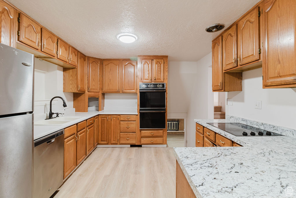 Kitchen with black appliances, light wood-type flooring, a sink, light countertops, and a textured ceiling