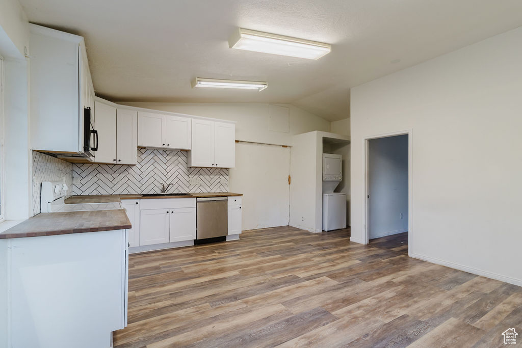 Kitchen featuring stacked washer / drying machine, dishwasher, vaulted ceiling, stove, and backsplash