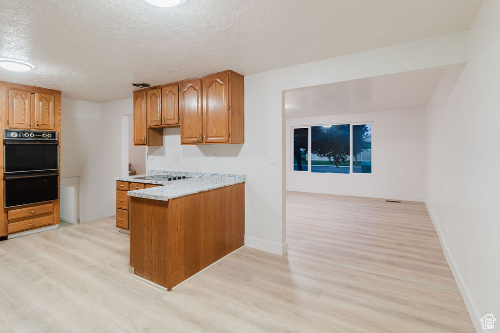 Kitchen featuring black appliances, light wood-type flooring, brown cabinets, and a textured ceiling
